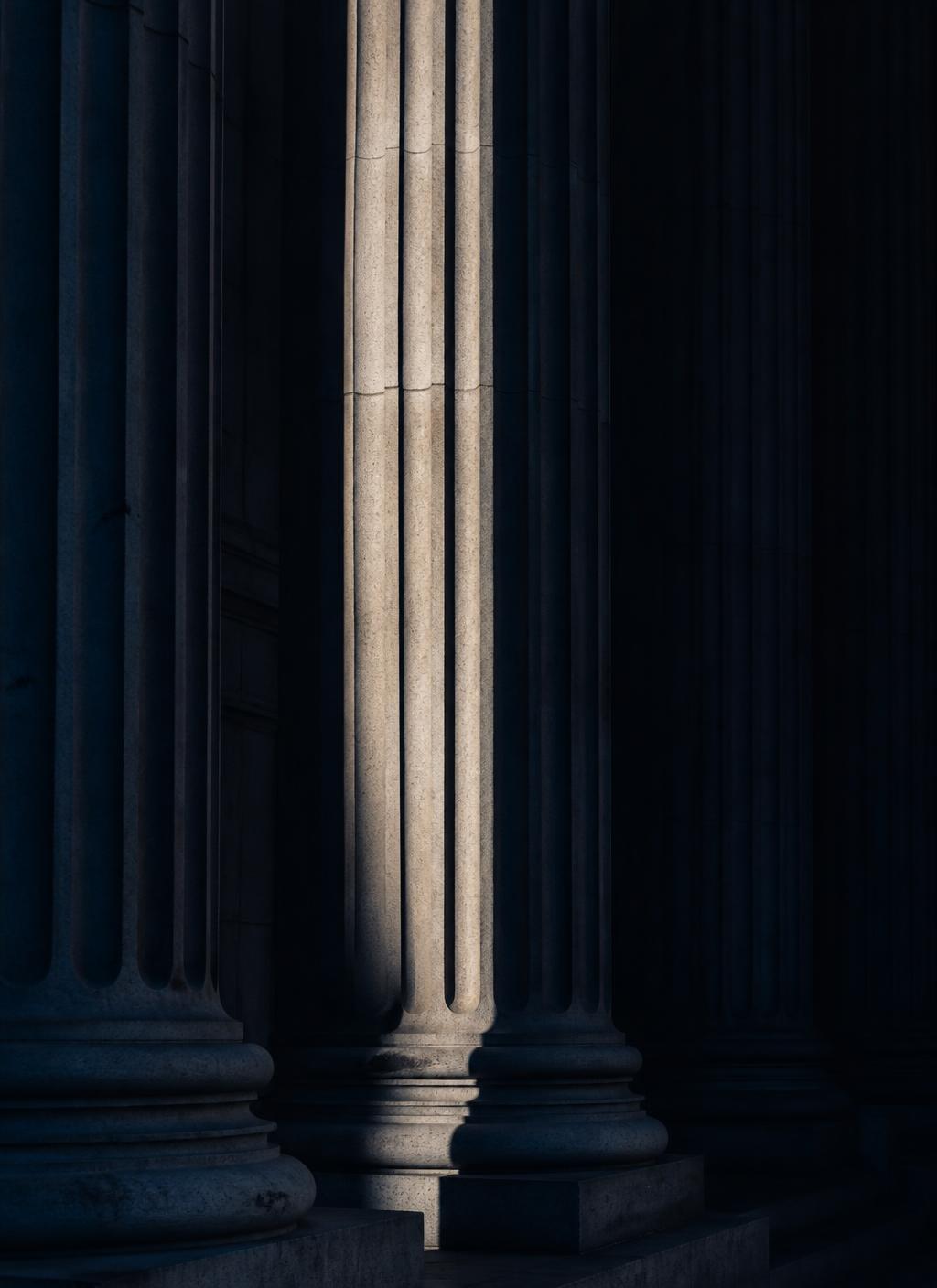 Sunlight raking across the stone columns of a courthouse portico